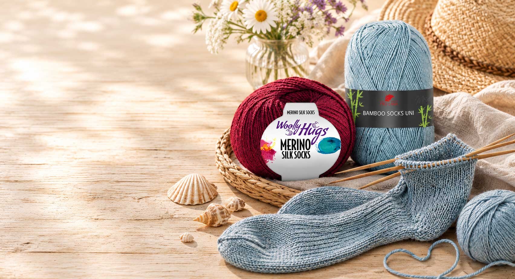 Sockenwolle und Stricknadeln auf einem Holztisch im Sommerlicht
